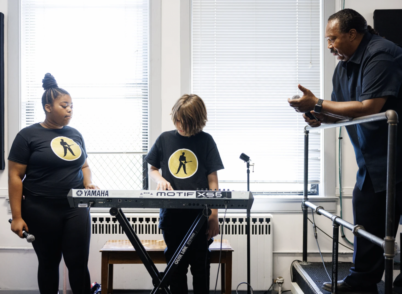 A teaching artist guiding young vocalists and a keyboard player